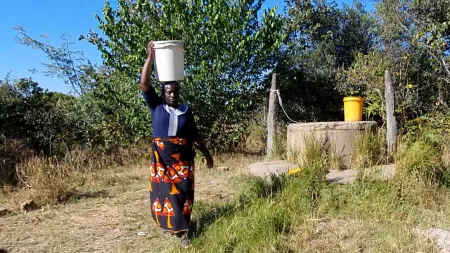 Zambia_Woman carrying a bucket of water on her head walking from well