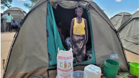 Zambia_Woman standing at the entrance of her tent with kitchen utensils and pap outside