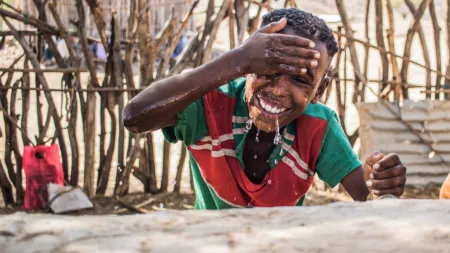 Ethiopia_Young boy i red and green shirt washing his face while smiling