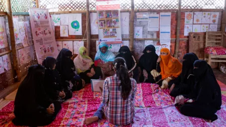 Rohingya_Women in niqabs sitting on the floor while other lady explains lesson from a book