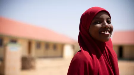 Somalia_Girl in red hijab smiling with school blurry in the background