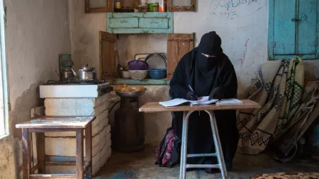 Syria_Woman in niqab sitting at desk writing next to stove