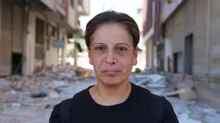 Turkiye_Woman with short hair and black t-shirt standing between blurry destroyed buildings