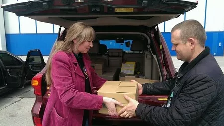 Ukraine_Woman in pink coat handing over box to man behind a car boot_CARE