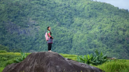 Girl on top of rock looking up in a green area