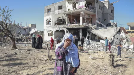 Palestinian woman covering her face in despair in front of a destroyed building.