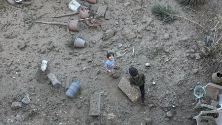 Boy looking up to the camera in destroyed area, with another boy walking