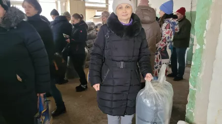 Woman with black coat and beige hat holding plastic bag with blue content