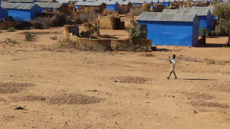 Child walking in dirt field with blue shelters in the background