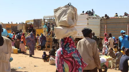 Woman's back carrying bags on her head in an arid space with spread out people