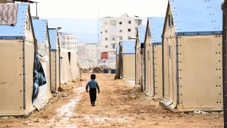 Boy walking in dirt road filled with tents