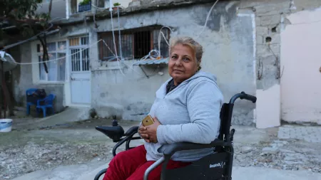 Blond woman sitting on wheelchair in front of buidling with broken window