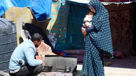 Woman holding baby and man cooking in cooktop placed on the floor.