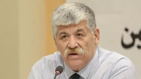 Man with white hair and moustache speaking on microphone