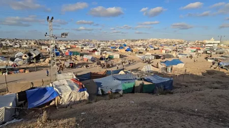 Tents in a wide camp. Sky is blue with some spreaded clouds.