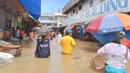 People wade through flood waters at a market in the Philippines, with vendors and customers navigating waist-deep brown water.