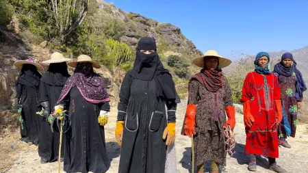Women wearing scarves and hats standing in arid area.