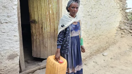 Woman with blue dress holding a jerry can in front of a door