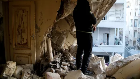 Person standing amid rubble and looking at destroyed wall