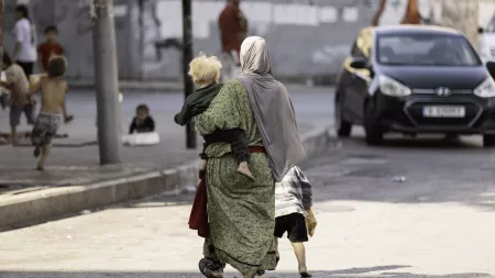 Back shot of woman carrying a baby while walking on the street