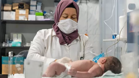 Nurse with purple scarf caring for baby lying on gurney