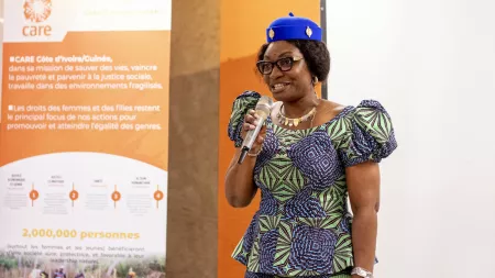 Woman wearing blue hat and patterned dress, speaking on a microfone