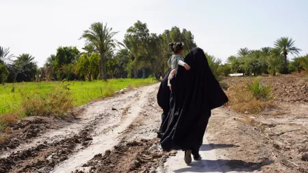 Back view of woman wearing black vest and scarf, holding a girl in her arms