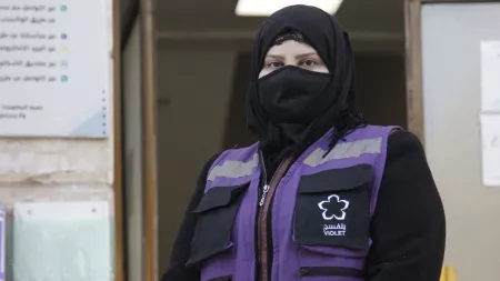 Woman wearing black head scarf and face cover and purple and black working jacket