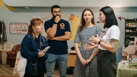 Three women and one man standing in a semi-circle chatting.
