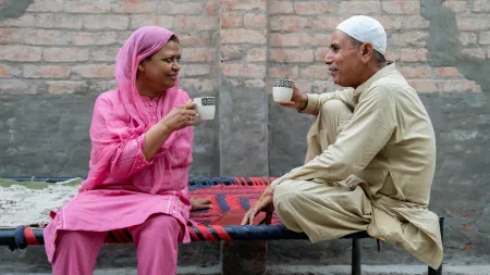 Woman and man facing each other holding tea cups while sitting on benches