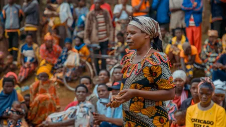 Woman wearing patterned dress and headscarf, speaking to crowd
