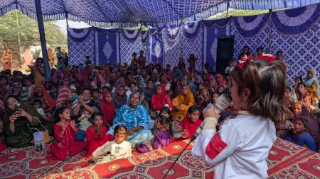 A girl takes center stage at a community event, raising her voice against violence experienced by women and girls.
