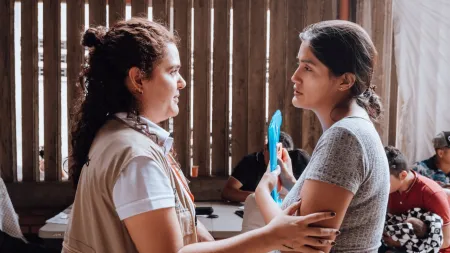 Two women facing each other. One gently holds the other's arm 