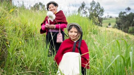 Girl in the forefront and woman in the background standing in a field, wearing hats and red ponchos.