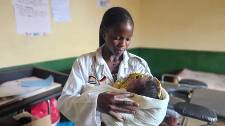 Woman wearing medical white coat holding a baby.