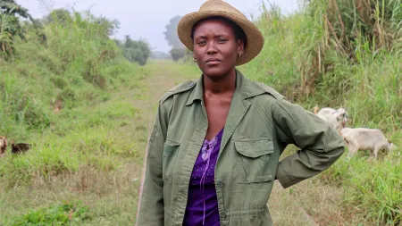 Woman standing on the field, wearing a hat, green jacket, and purple shirt.