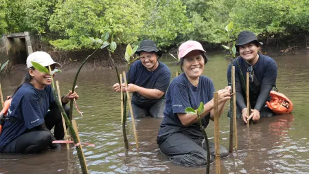 Women wearing dark shirt, pants, and hats standing in water and smiling to the camera.