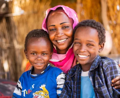 A Sudanese woman smiles with two young kids.