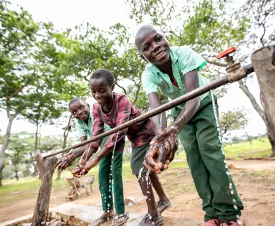 Three kids wash hands from a tap water station.