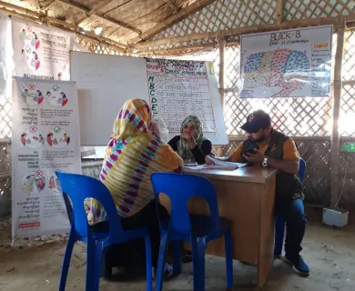 Three people sit at a desk together and review feedback. There are large papers on the nearby walls showing handwritten comments about CARE feedback.