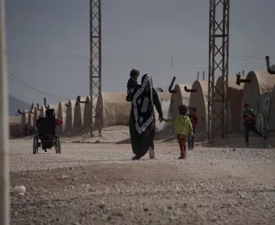 Woman walks in IDP camp with two children