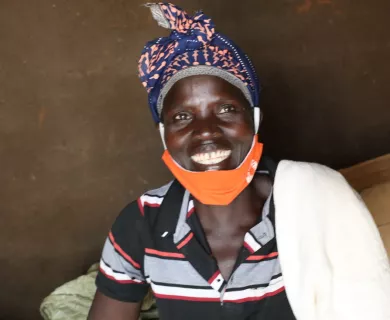 A woman smiles. She has an orange face mask pulled down so that her smile is visible.