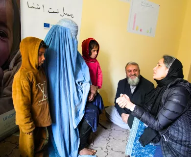 Woman in burqa with her two children speaking with woman kneeling holding her hands and man sitting in the floor in the background