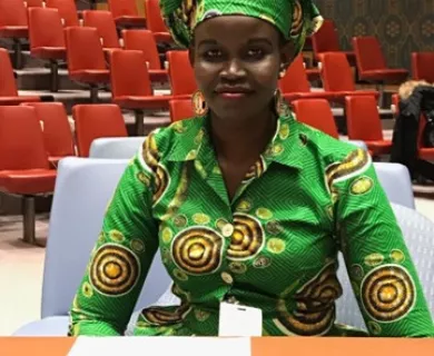 Woman with half smile wearing green and yellow head wrap and dress