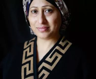 Woman with half smile, wearing dark headscarf with patterns in grey