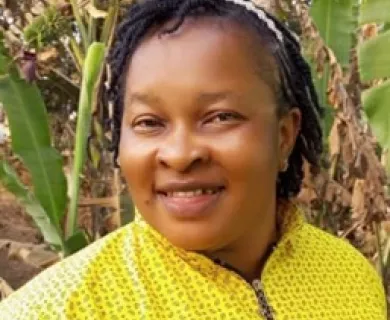 Headshot of woman smiling, with short black braided hair. Wearing yellow shirt with patterns
