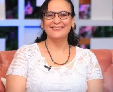 Woman with dark hair pulled back, glasses, sitting in a chair smiling to the camera