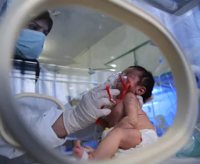 midwife is using a nebulizer on a newborn baby inside the incubation section 