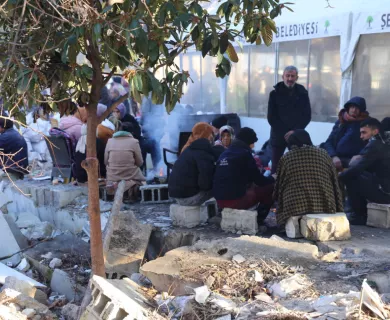Turkiye-Syria_Groups of people sitting on bricks outside tent shelter