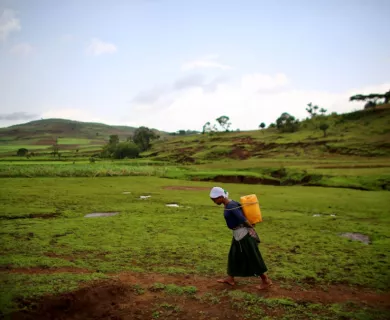 Ethiopia_Woman walking with yellow water can through lush hill area
